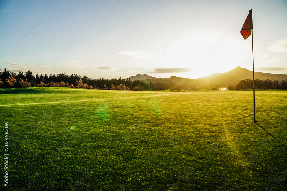The flag on the ninth hole green with the sun rising behind distant hills