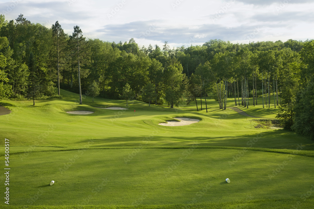 View from the tee of a par 3 with sand bunkers around the green and woods behind